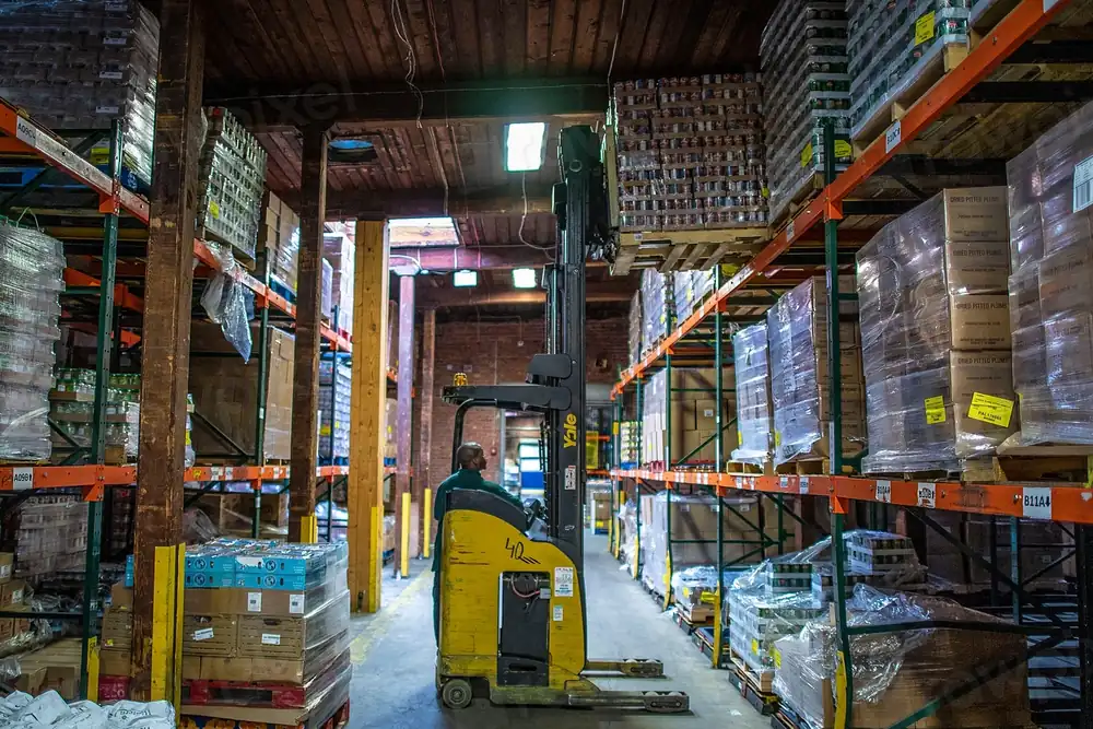 A worker moving pallets in a stocked warehouse
