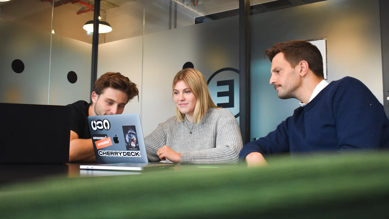 Three colleagues reviewing work together on a laptop in a meeting room