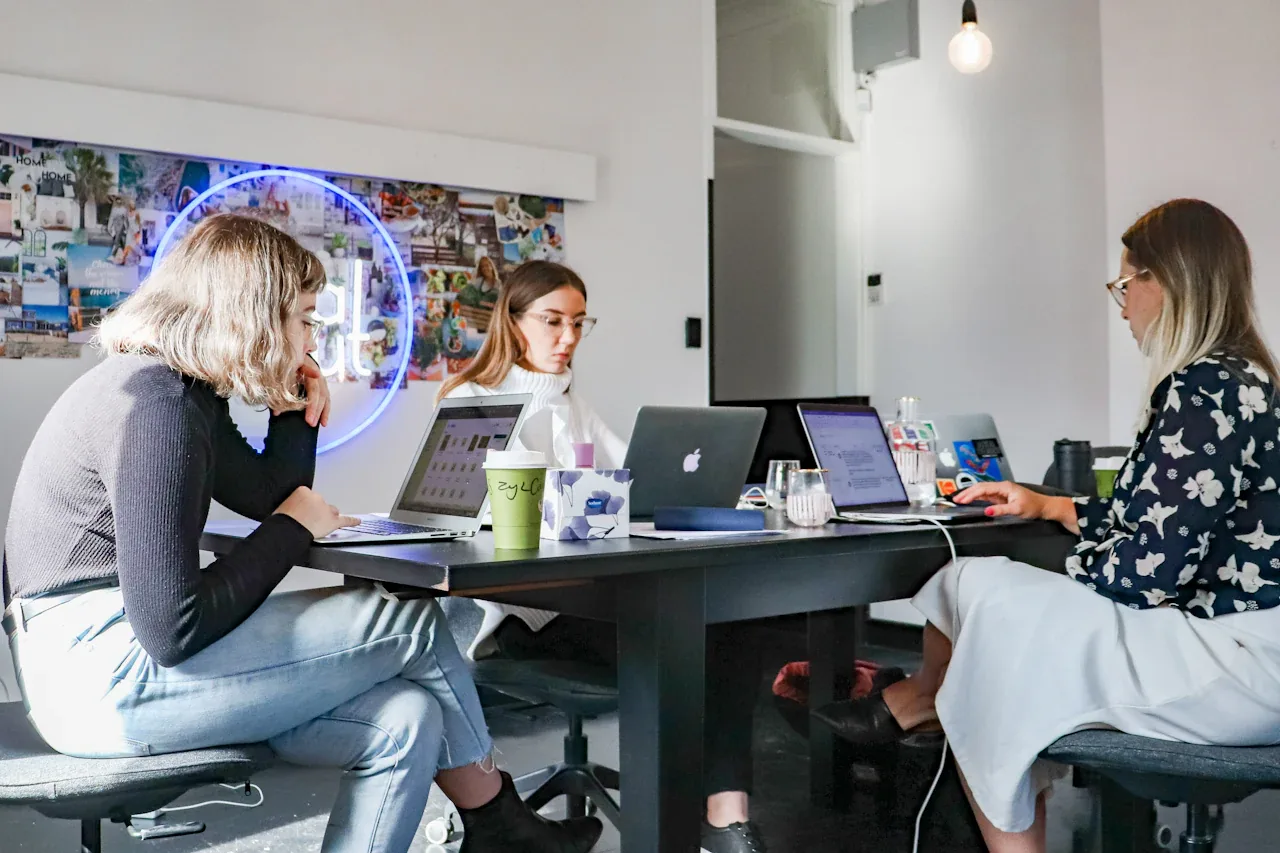 Three colleagues working on laptops at a studio table in front of a moodboard wall