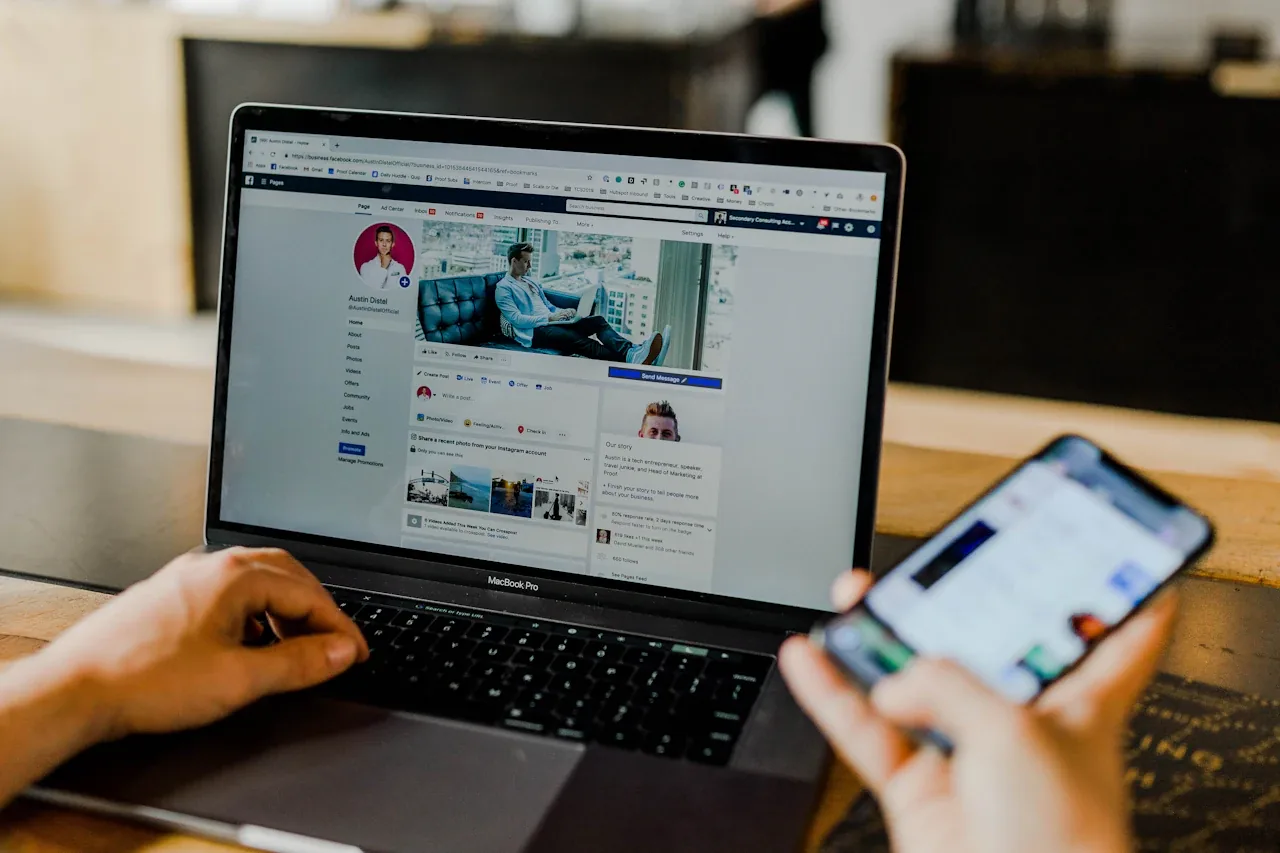 Laptop showing a Facebook business page manager while a person holds a phone