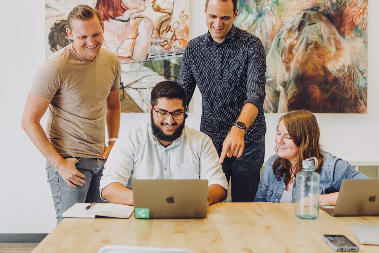 Four colleagues gathered around a laptop in an office, reviewing work together